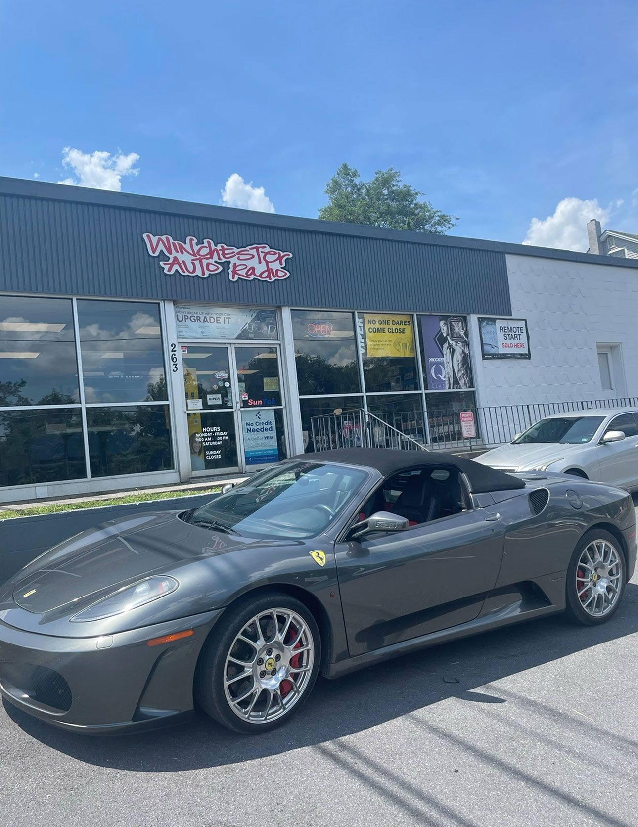 Gray Ferrari convertible parked outside a car shop on a sunny day