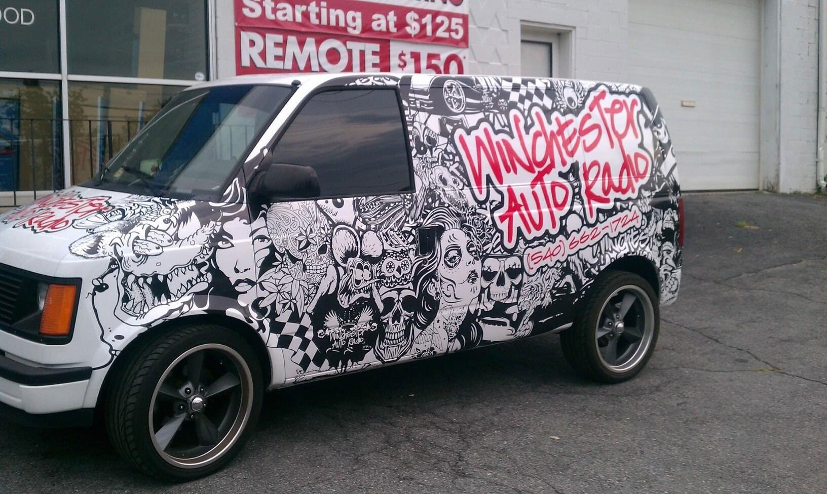 Black SUV with white-and-pink graffiti-style wrap parked outside a shop.