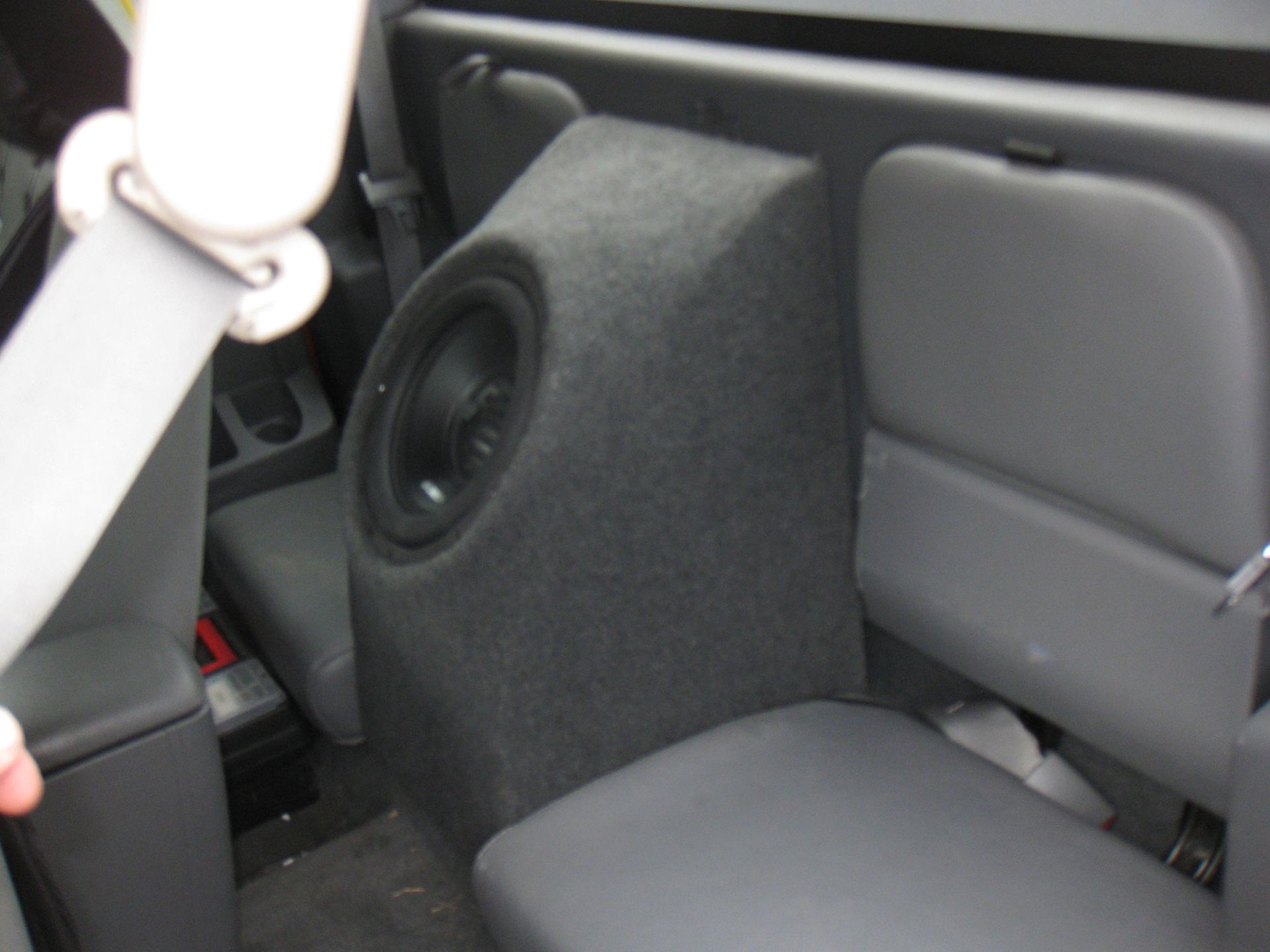 Car interior with a large black subwoofer mounted beside the rear seat.