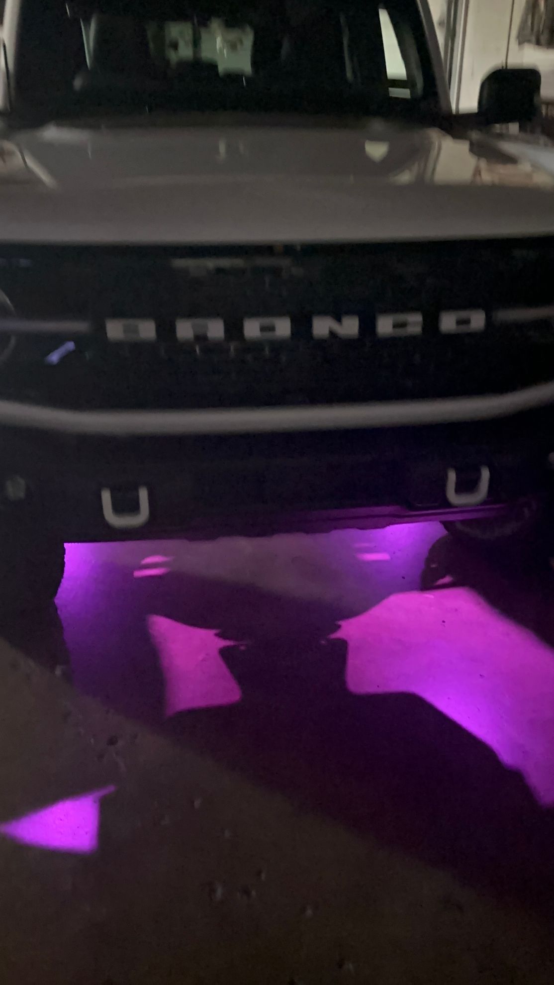 Front of a black Bronco with purple underglow lighting on pavement at night