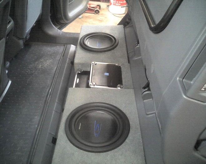 Car interior with custom subwoofer speakers and a phone on a gray center console.