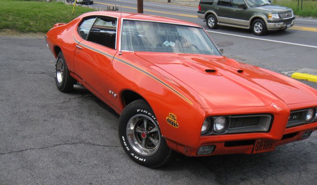 Orange classic muscle car parked outdoors on pavement, shown from the front-left side.