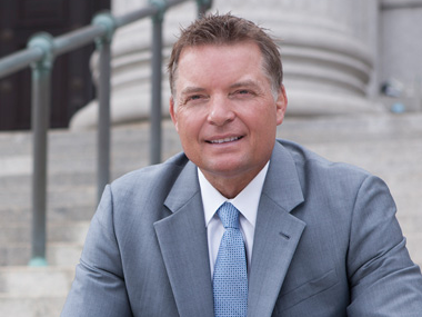 Man in a gray suit smiling outdoors on steps near a building