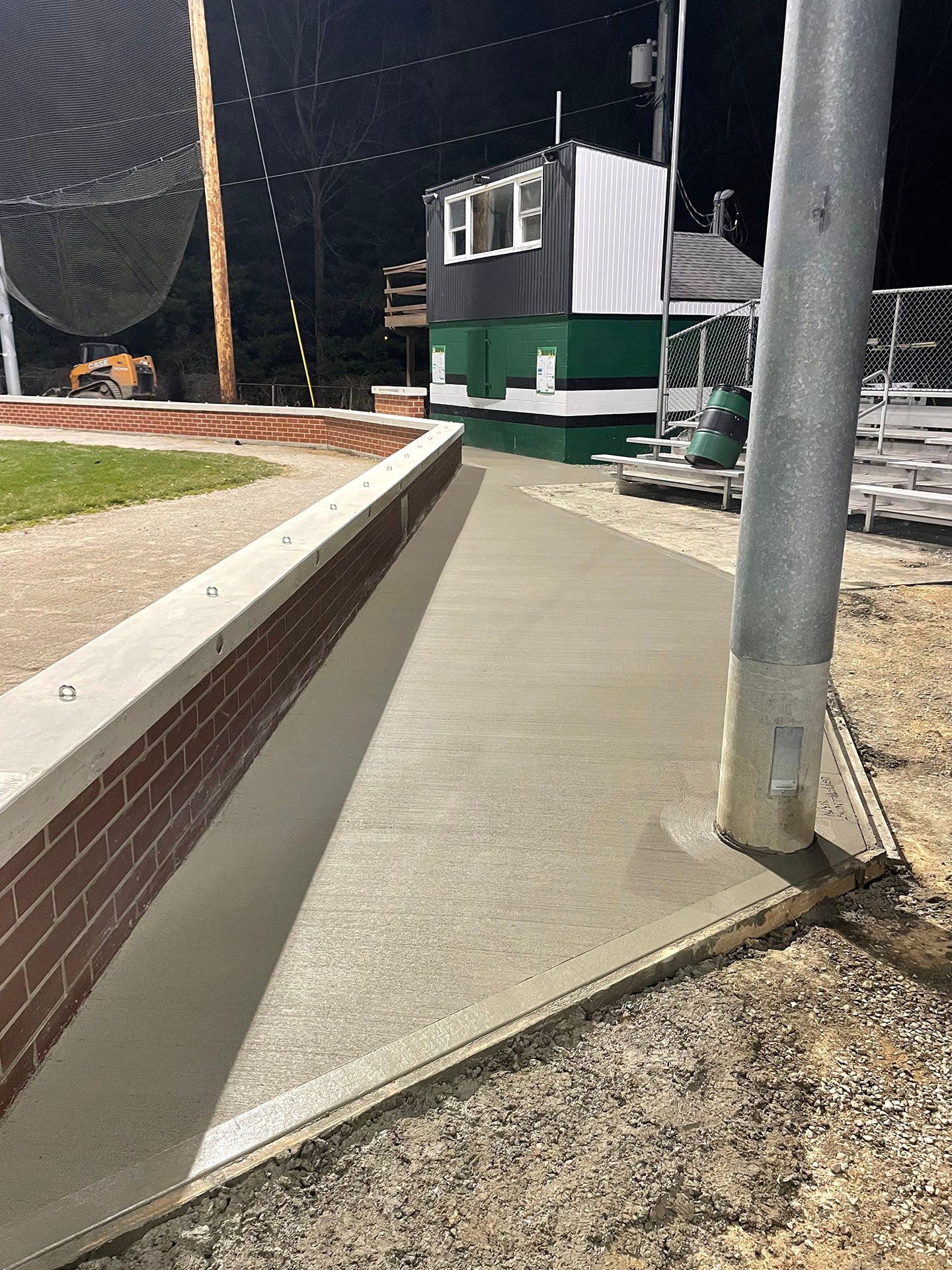 A concrete walkway leading to a baseball field at night.