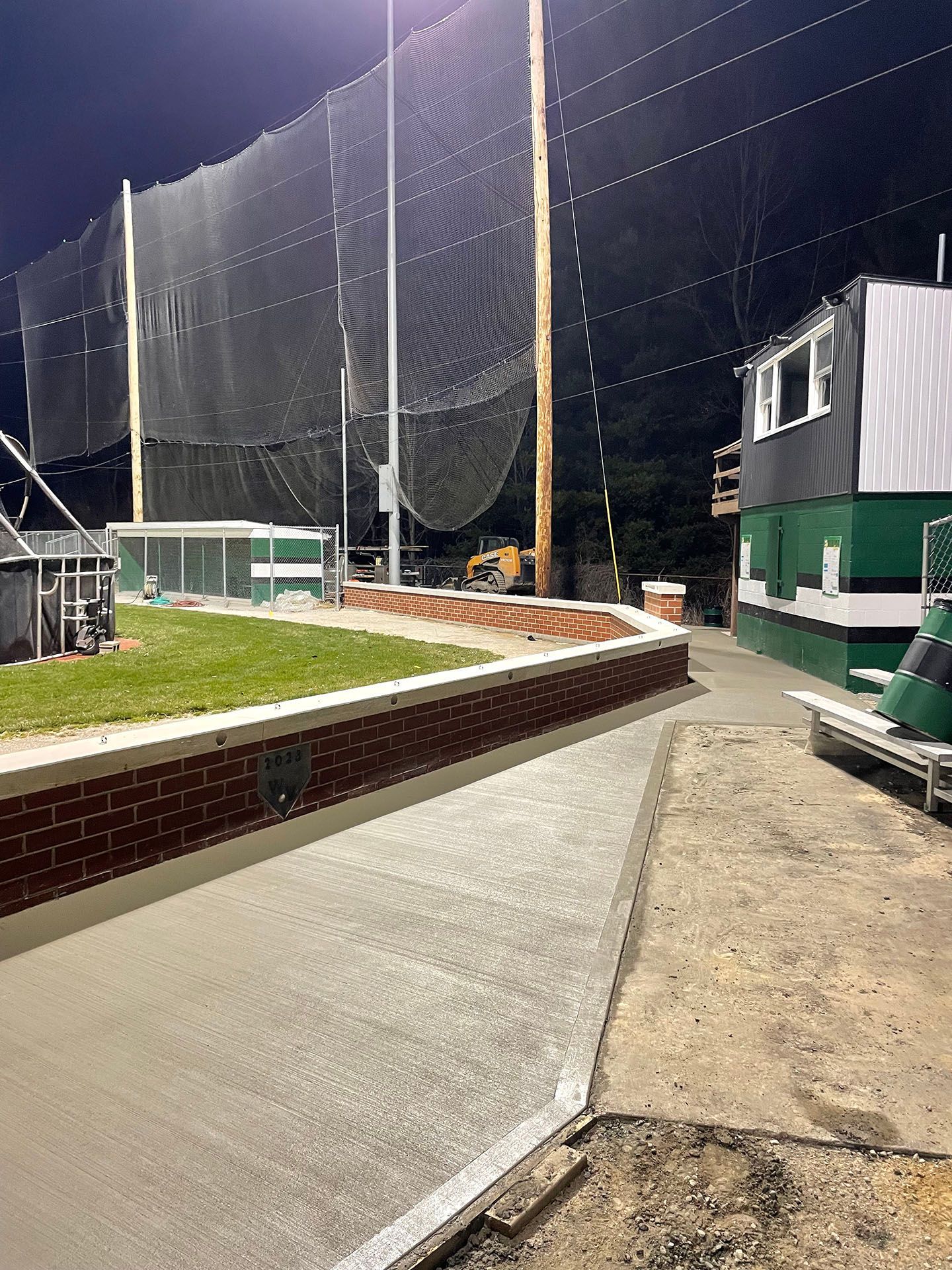 A baseball field with a fence and a building in the background at night.