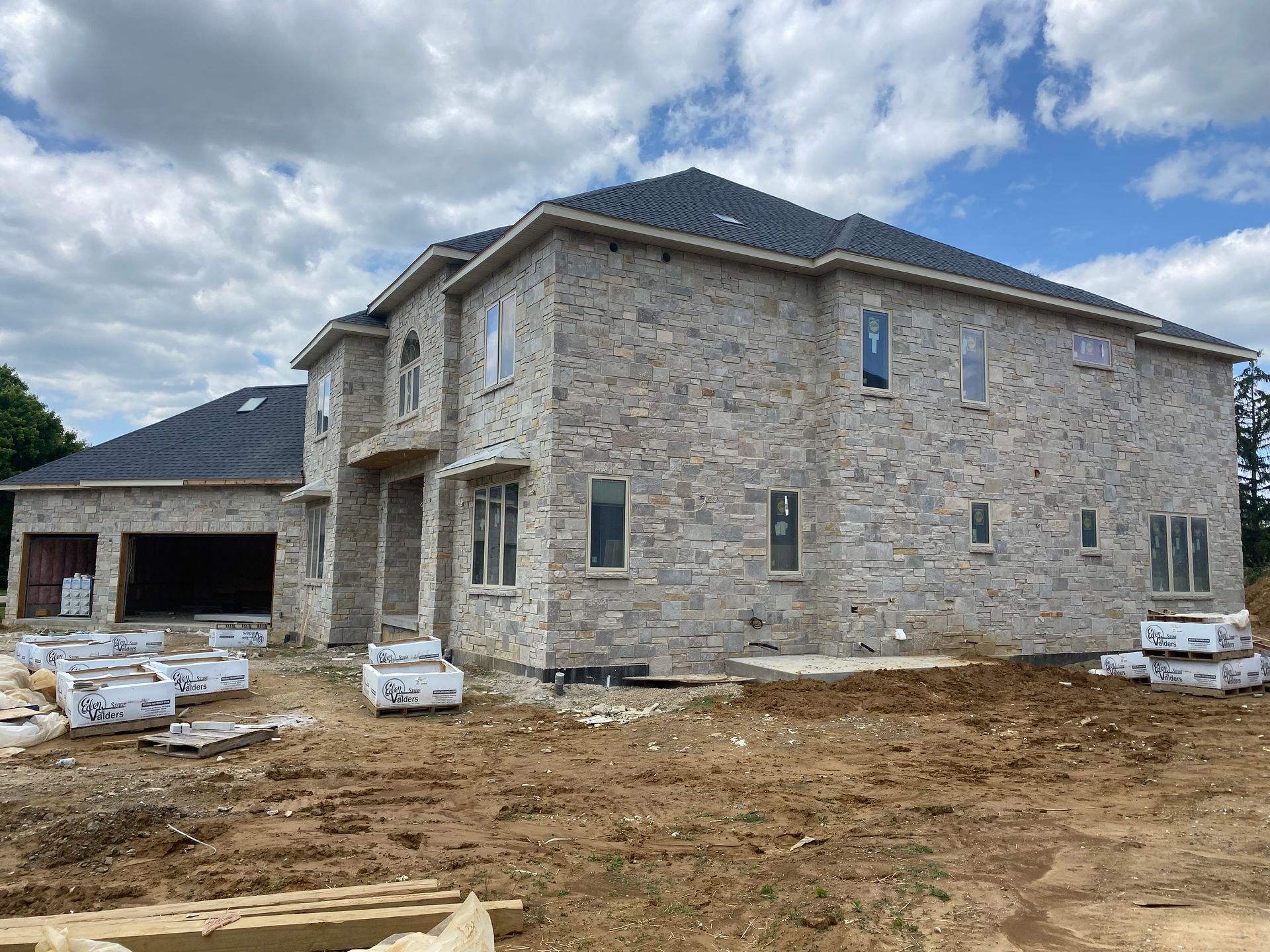 A large brick house is being built in a dirt field.