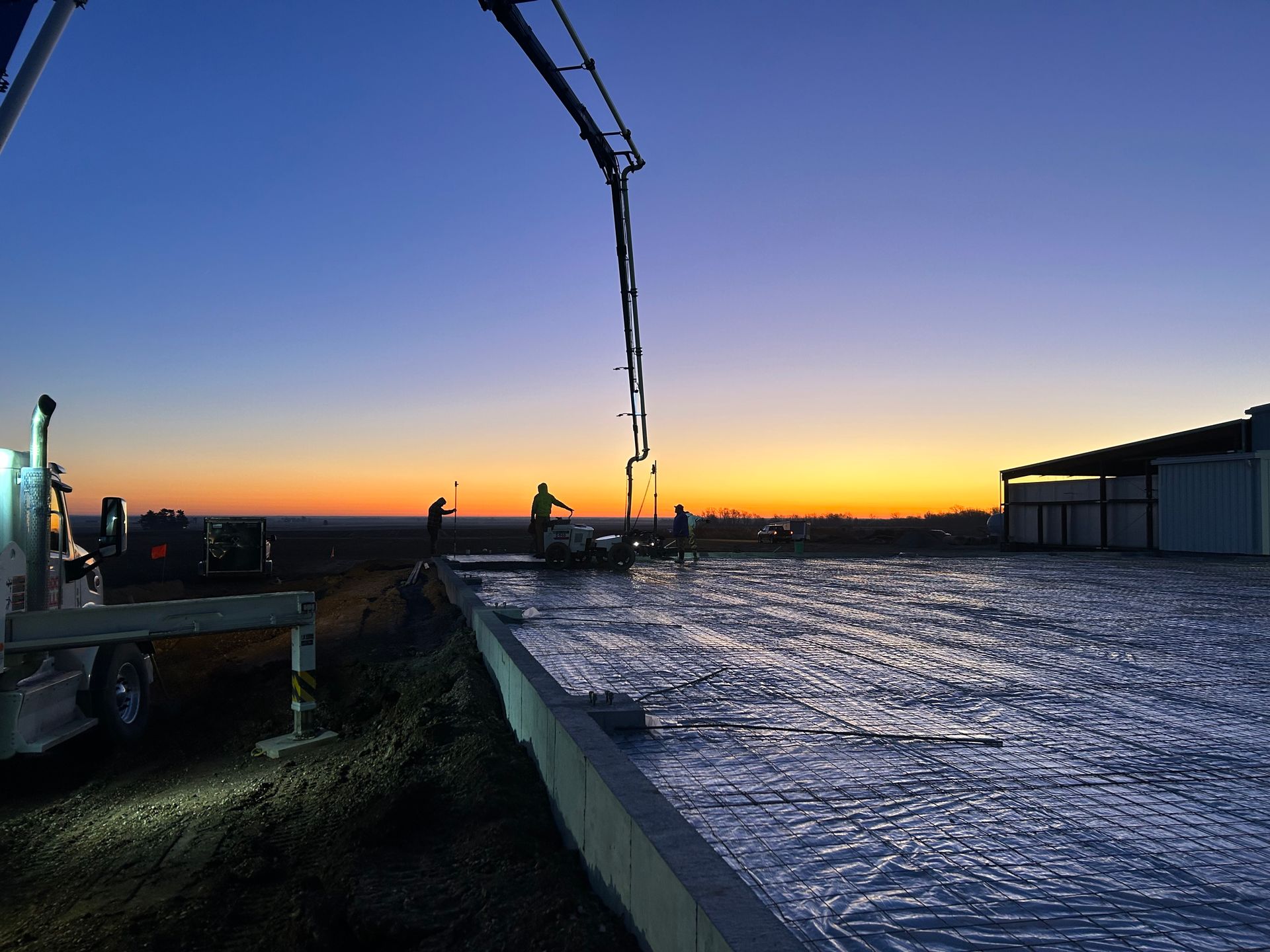 A crane is pouring concrete on a roof at sunset