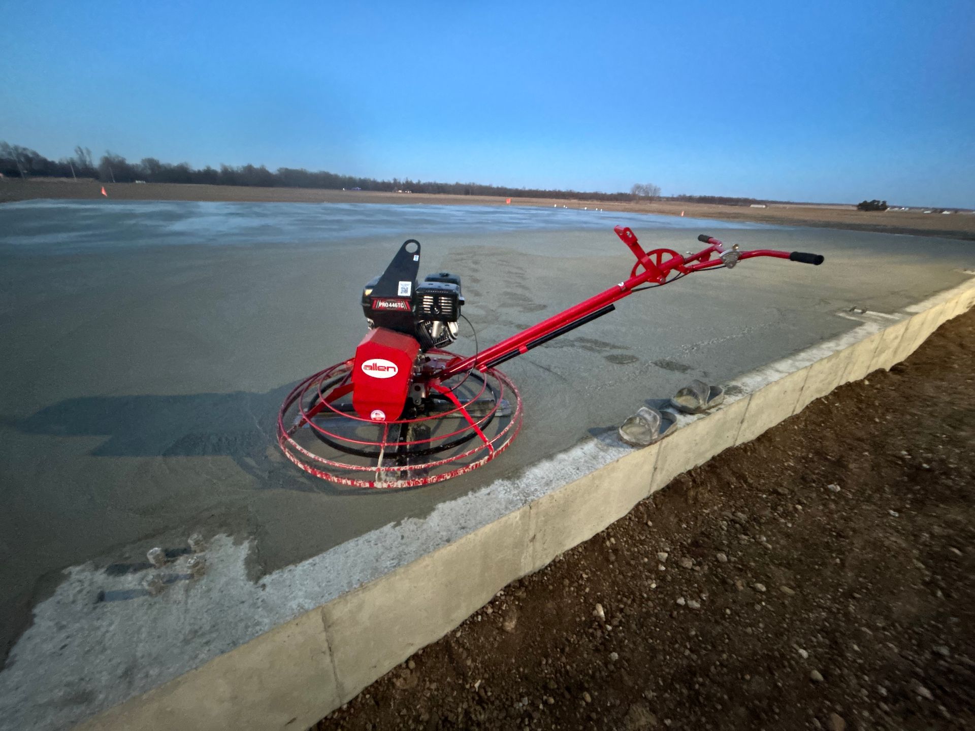 A red concrete trowel is sitting on top of a concrete surface.