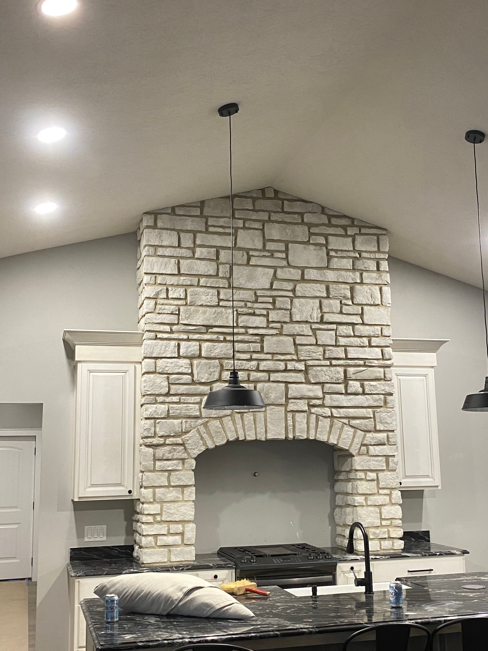 A kitchen with a stone fireplace and white cabinets.