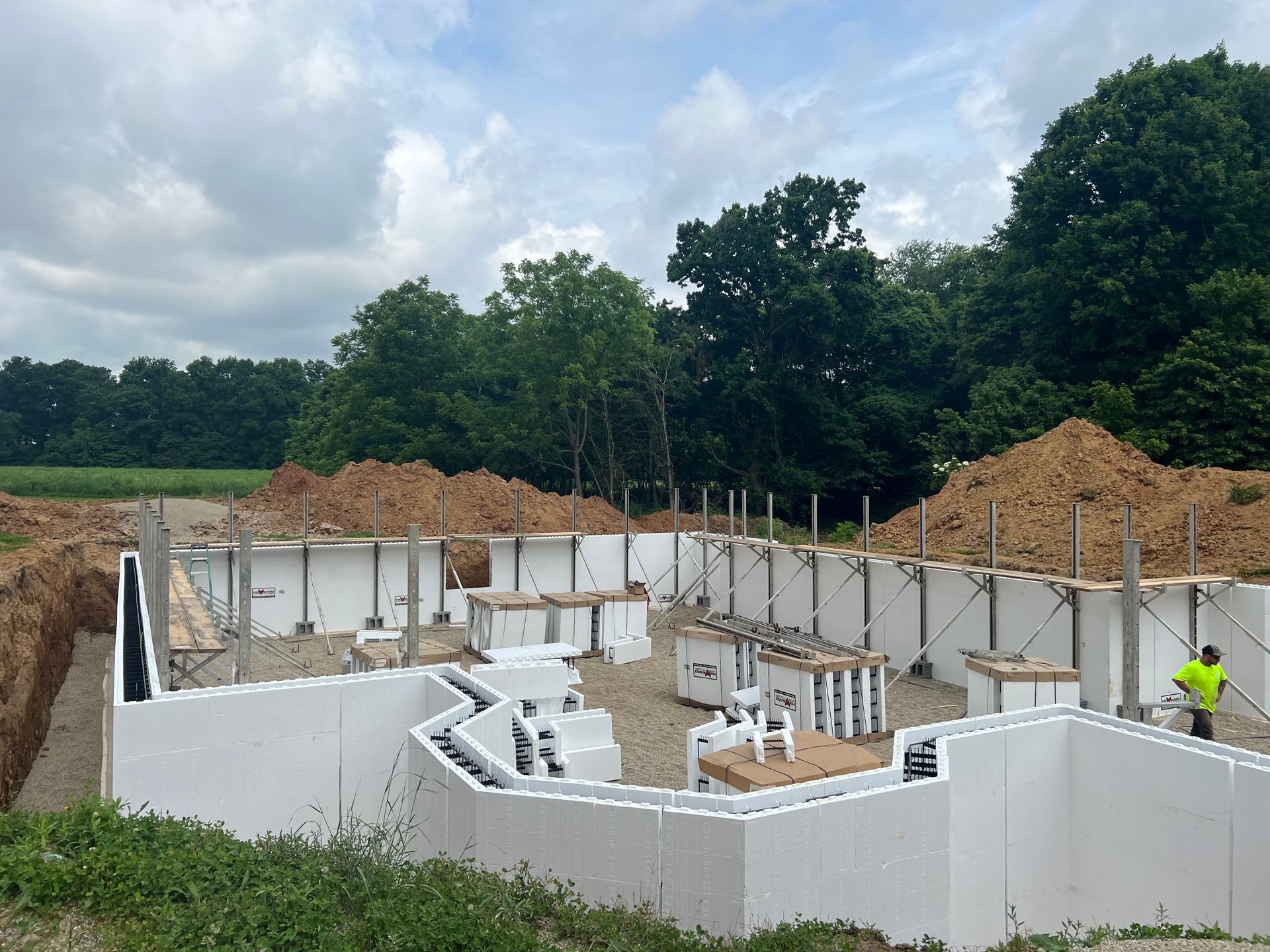 A man in a yellow vest is standing in front of a building under construction.