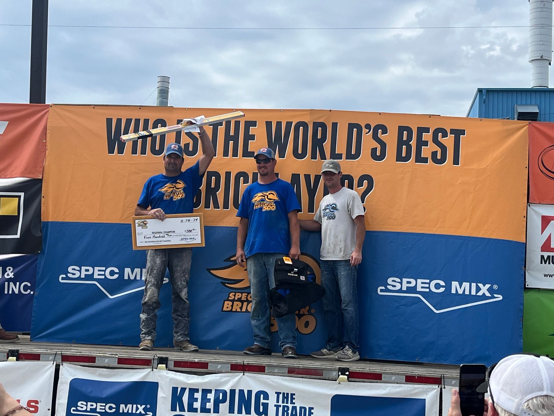 Three men stand on a stage in front of a banner that says