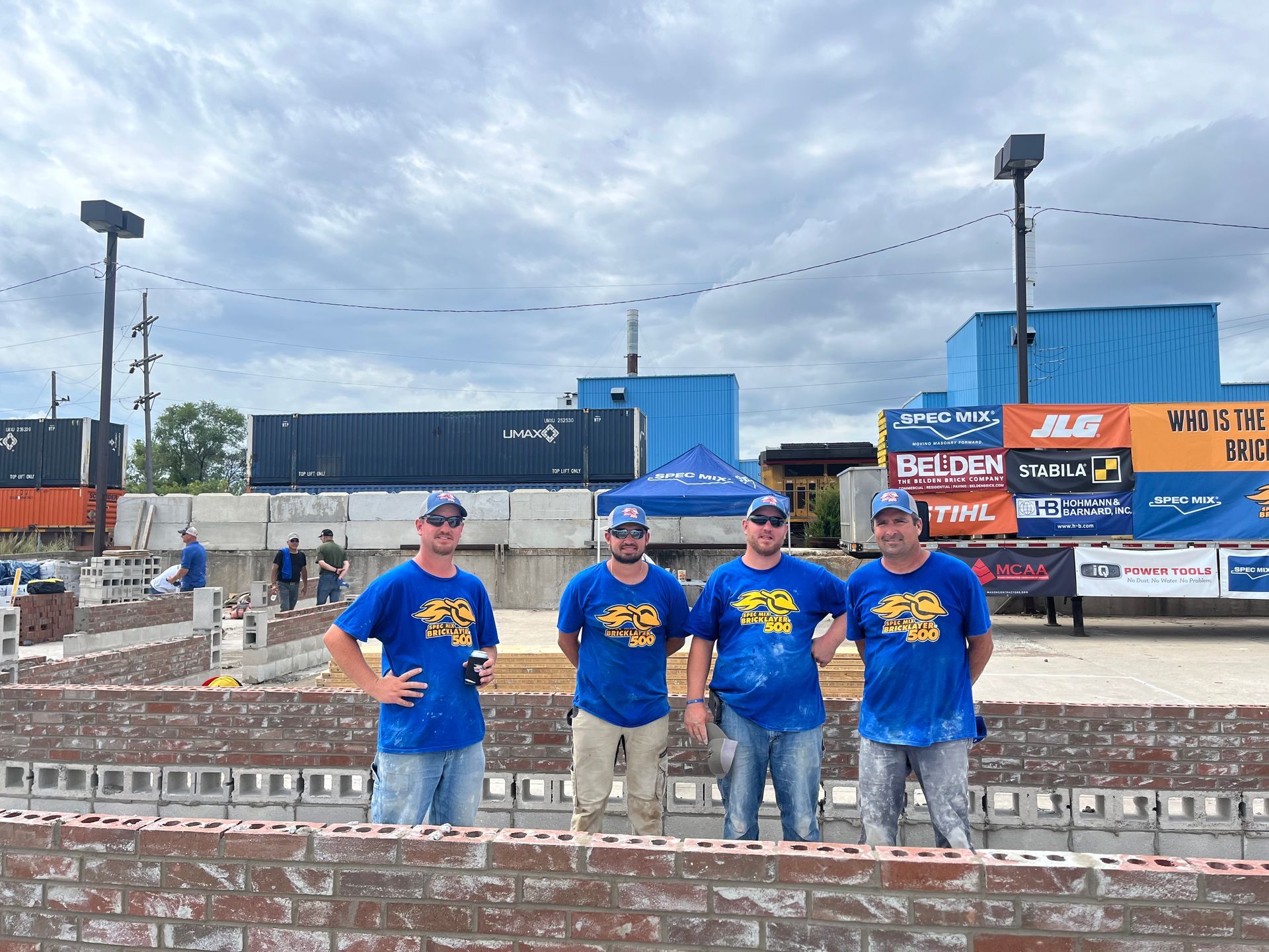 A group of men wearing blue shirts are standing in front of a brick wall.
