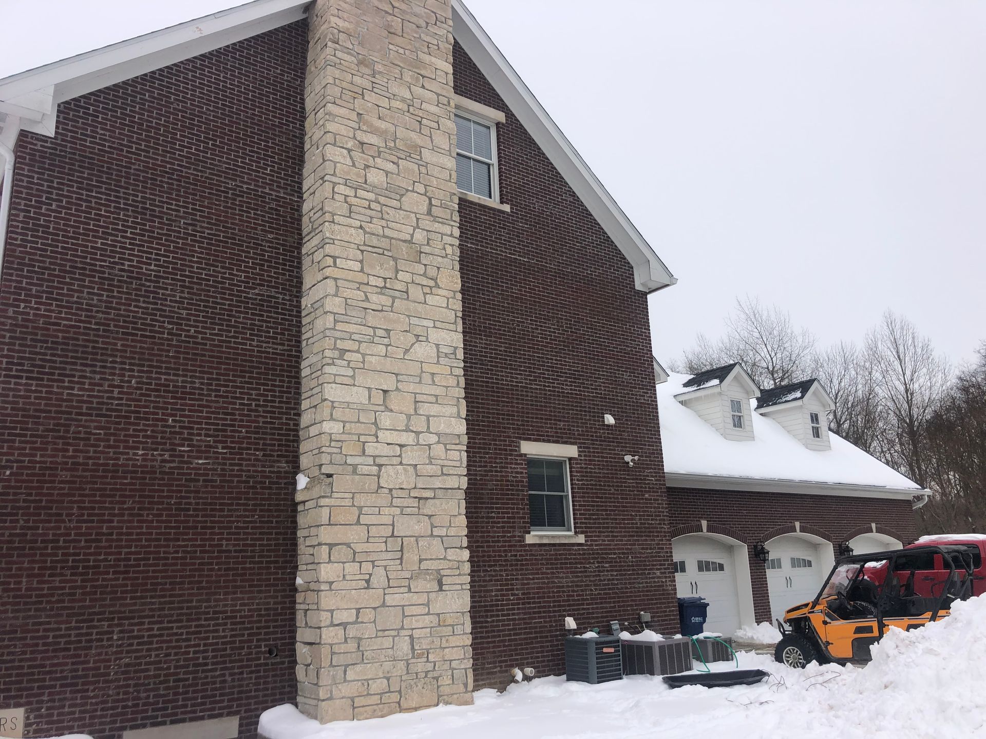 A brick house with a stone chimney is covered in snow.