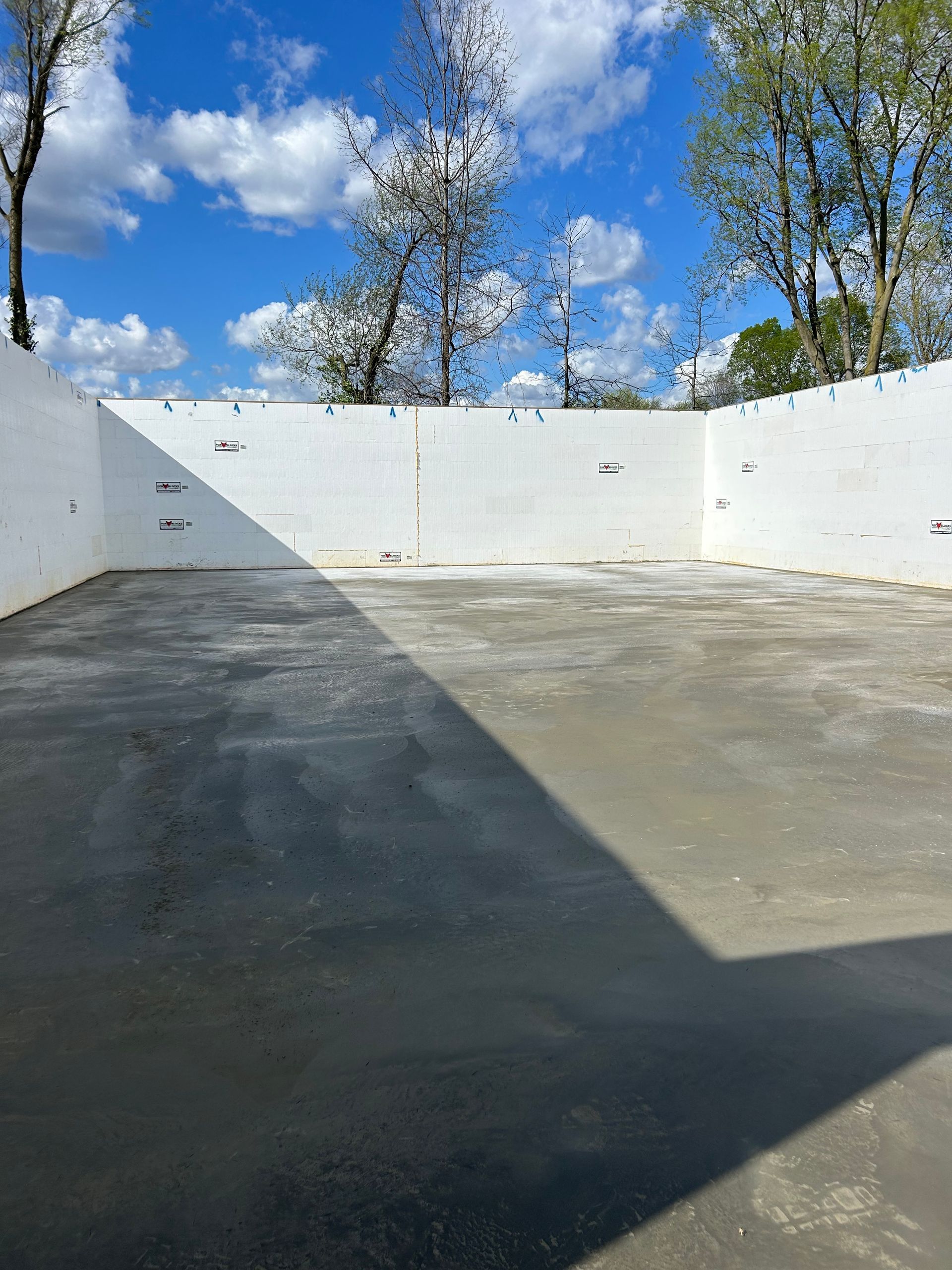 A large concrete area with a white wall and trees in the background.