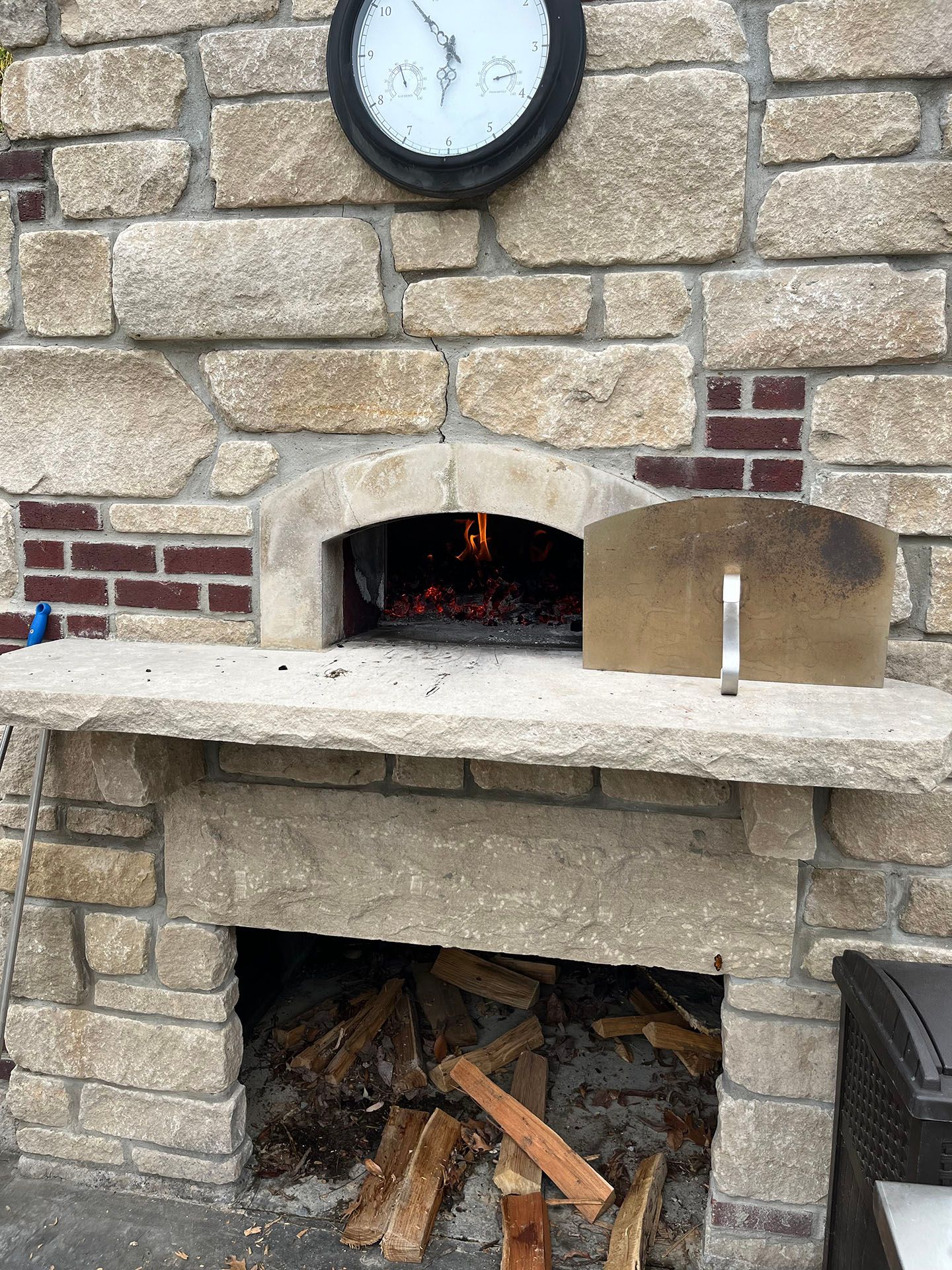 A pizza oven is being cooked in a stone fireplace with a clock above it.