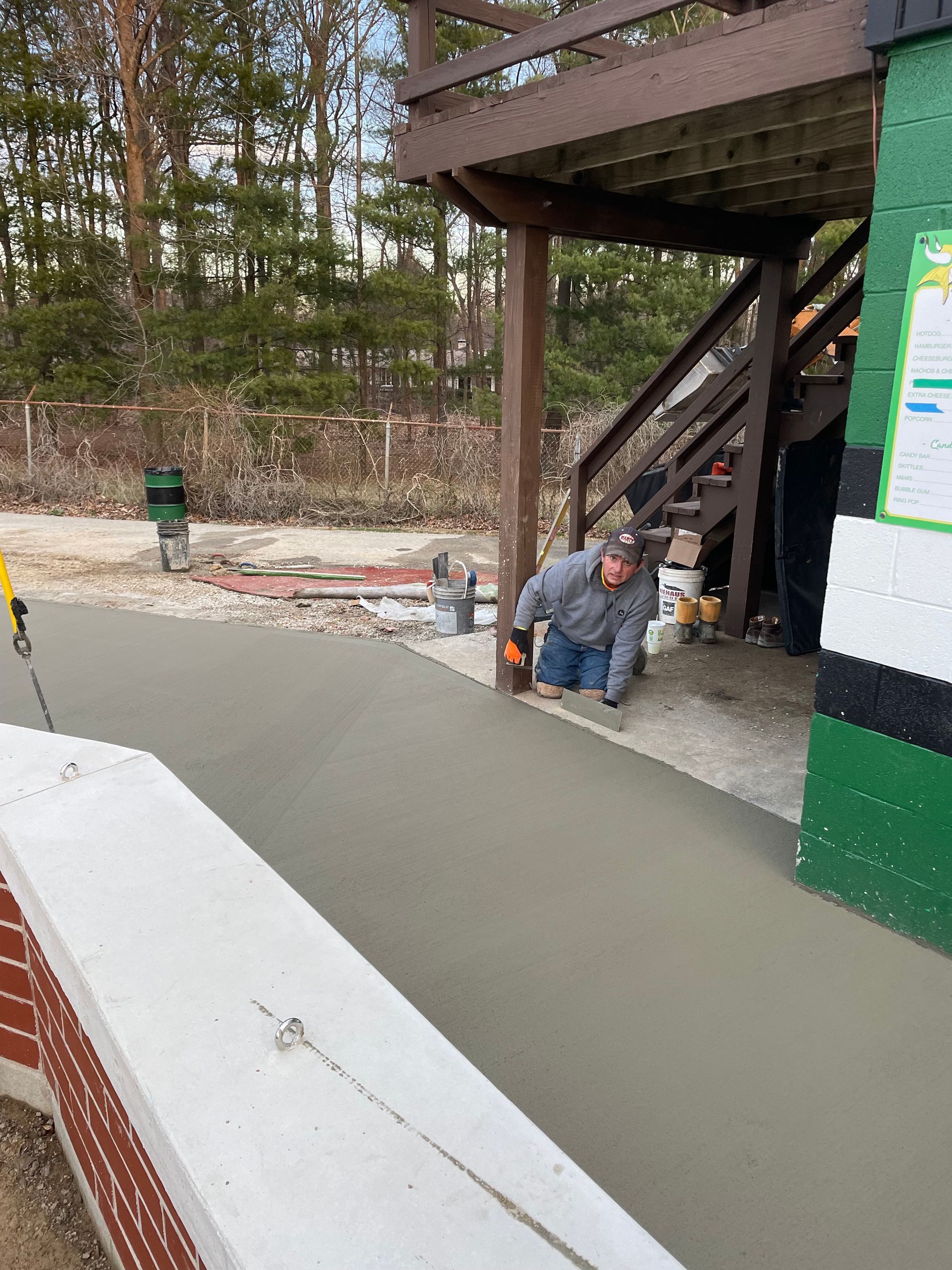 A man is working on a concrete walkway in front of a green building.