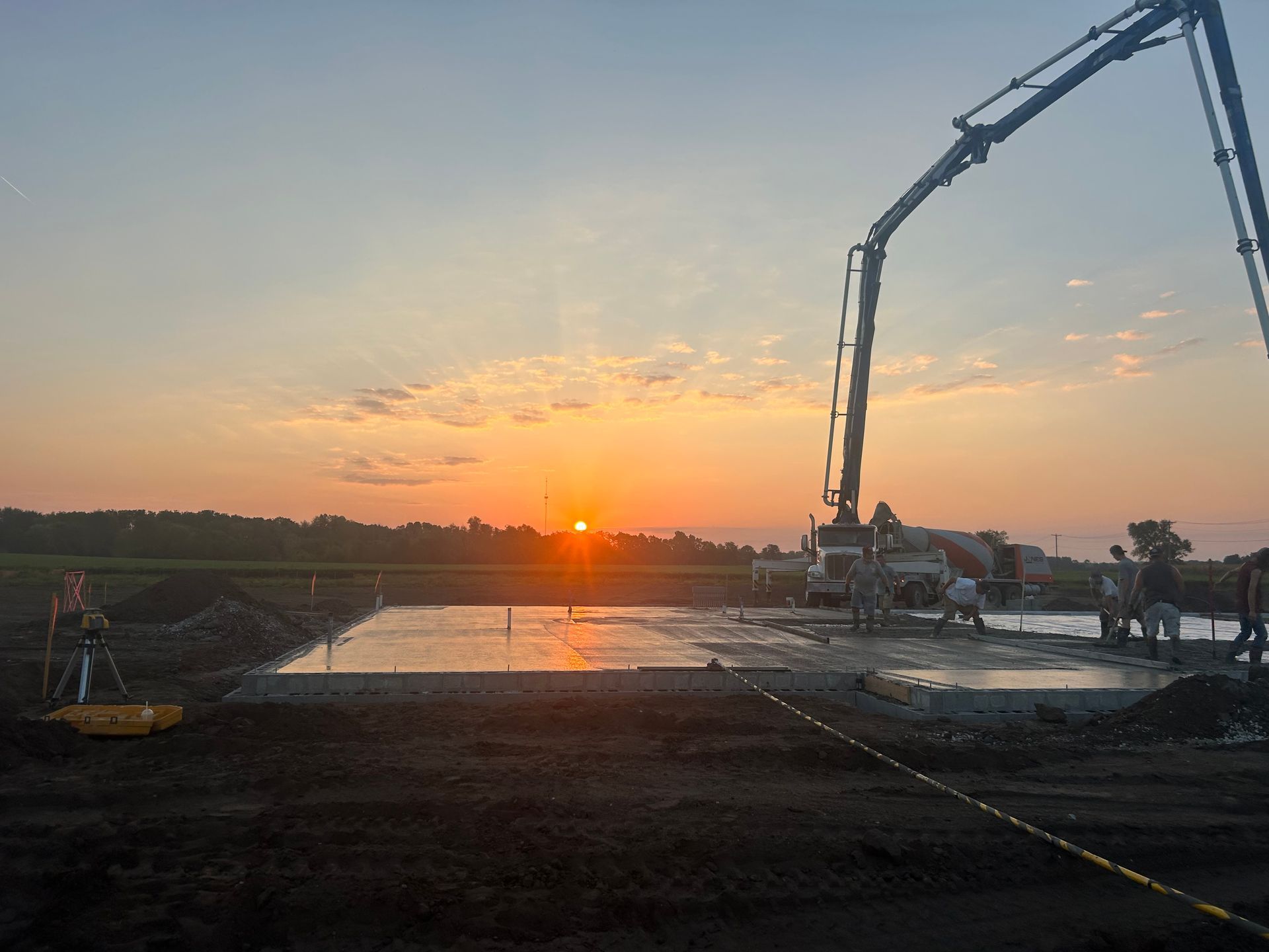 A concrete pump is pouring concrete on a construction site at sunset.