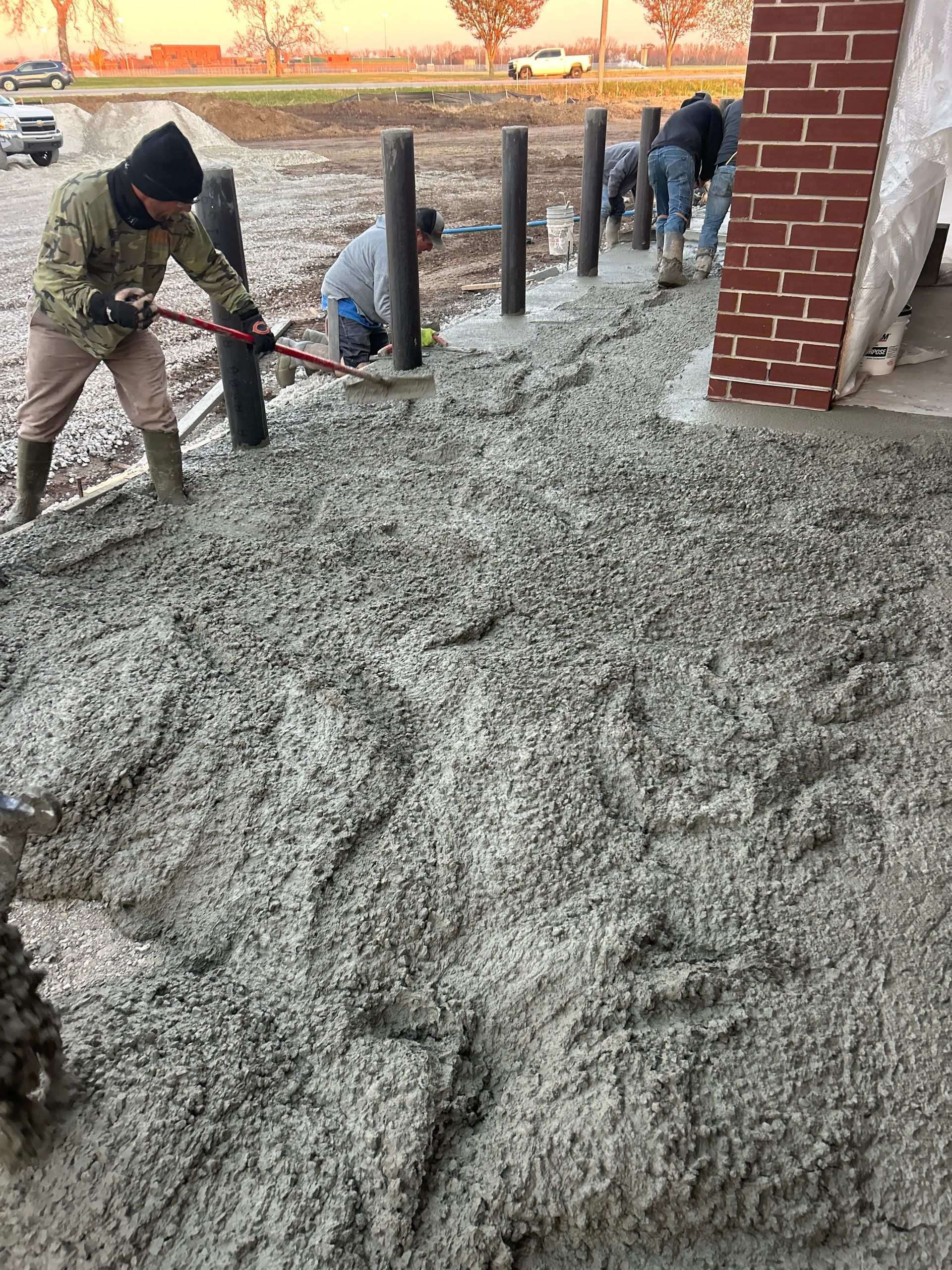 A man is pouring concrete on a sidewalk in front of a brick building.