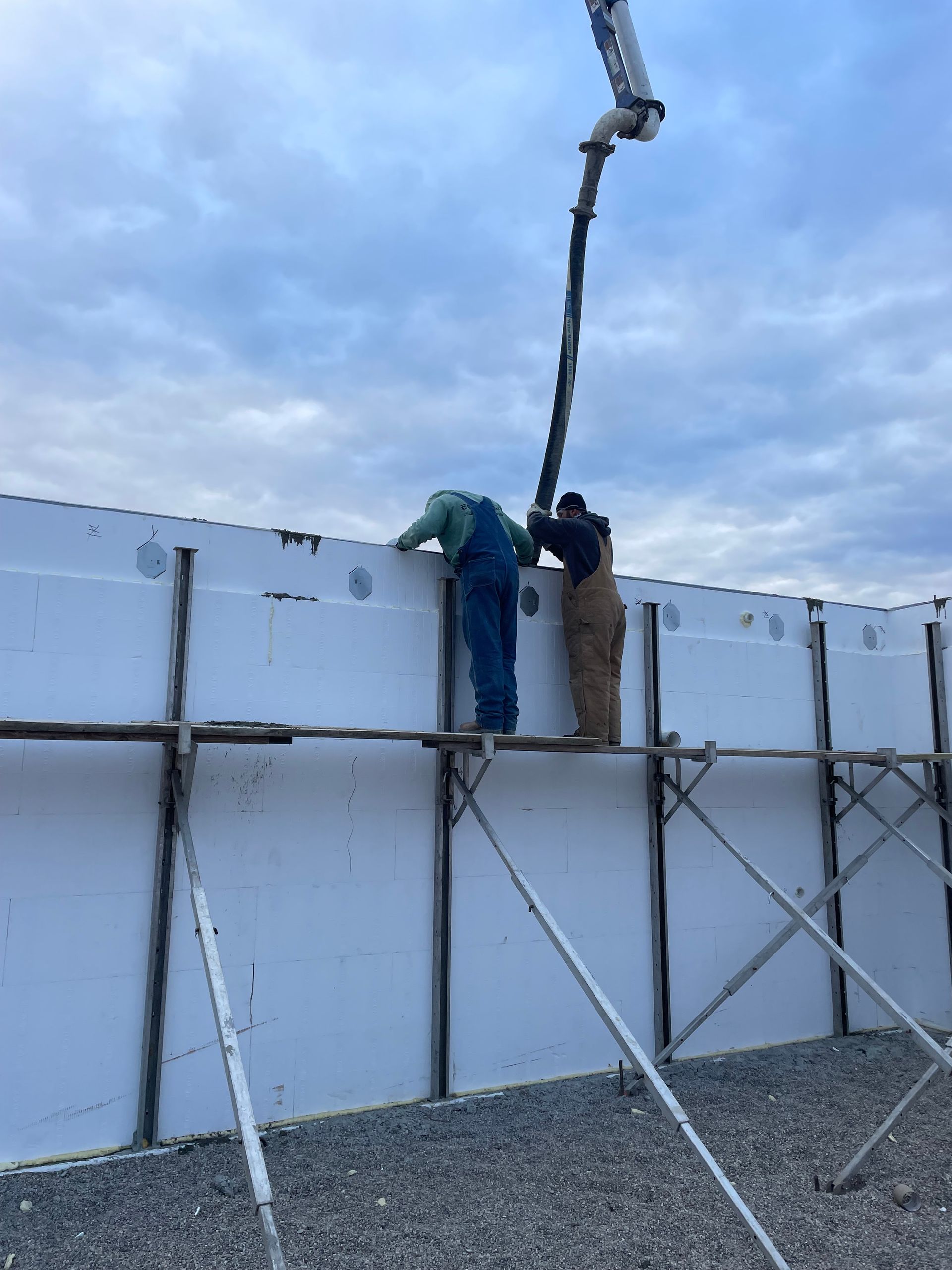 Two men are working on a wall with a concrete pump.