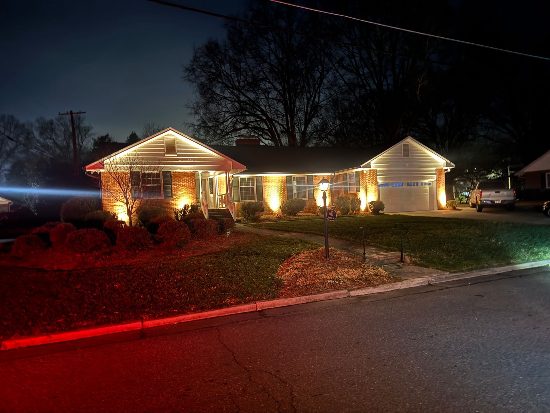 House at night with white Christmas lights on the roof and shrubs illuminated by warm lights.