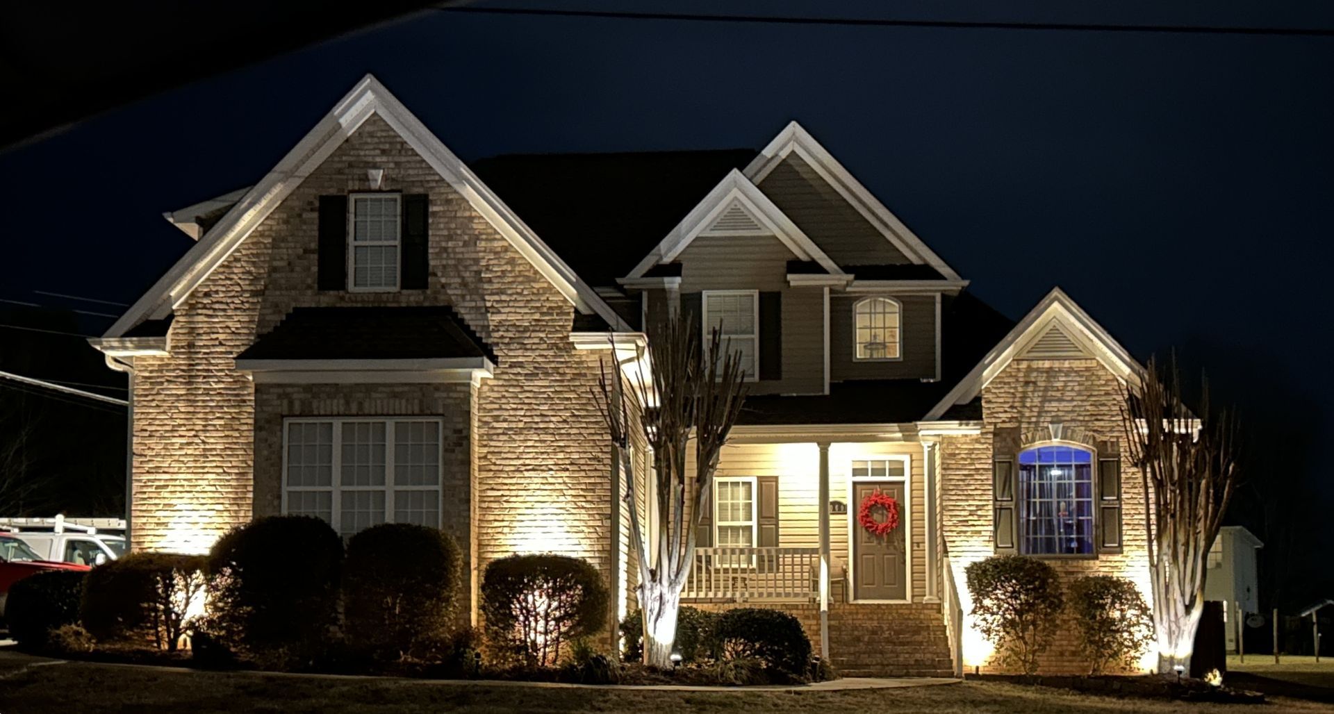 House illuminated at night with spotlights, showing brick facade and landscaping.