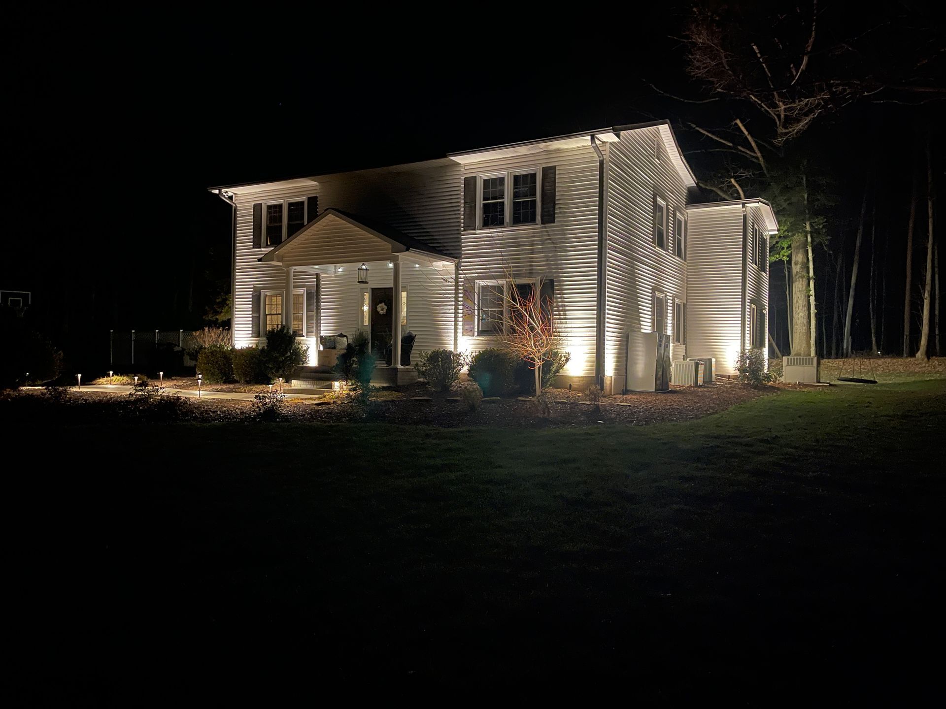 Two-story white house at night, illuminated by spotlights on a dark lawn.