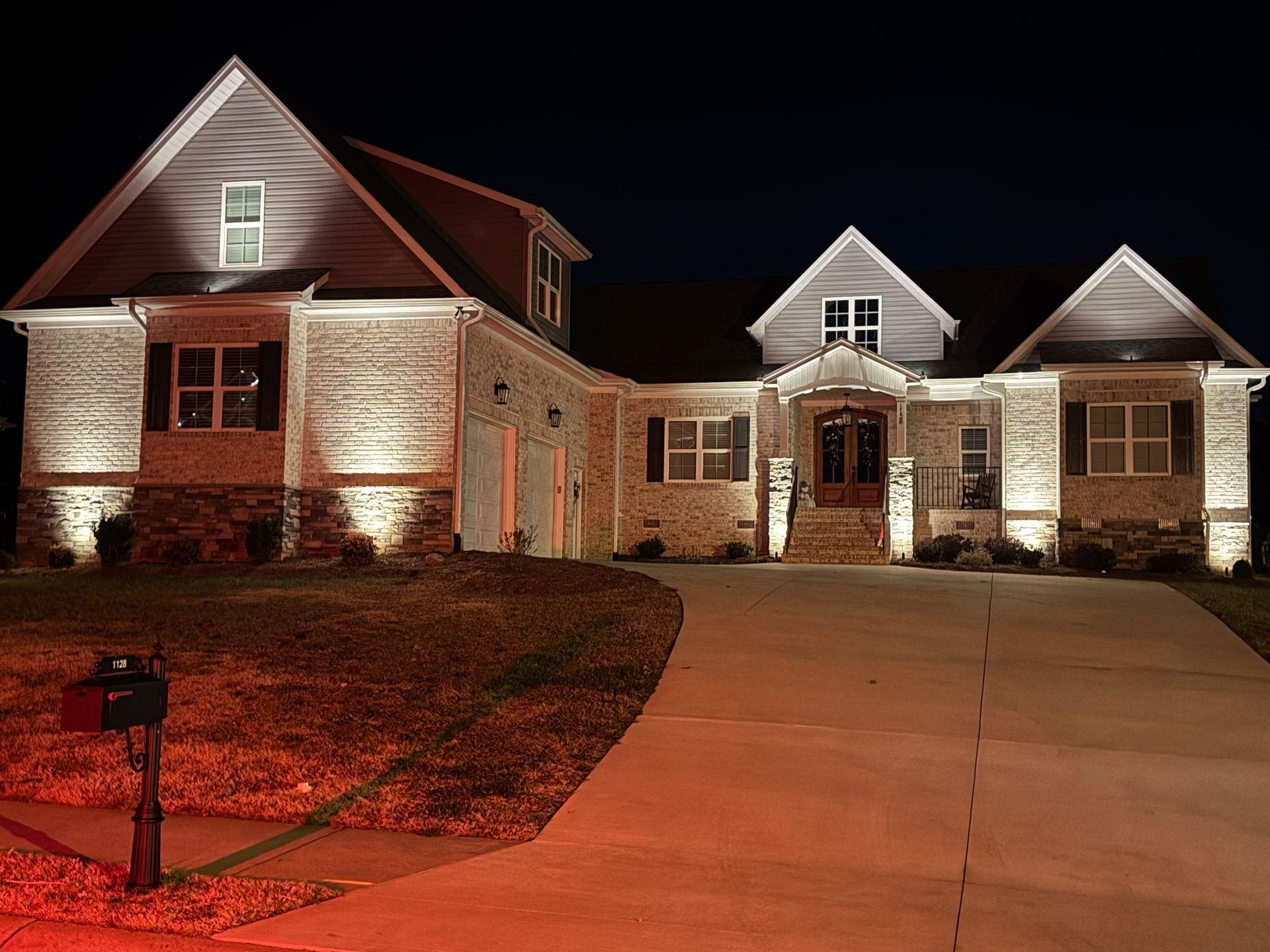 Night-lit two-story house with brick and siding, illuminated driveway, and front door.