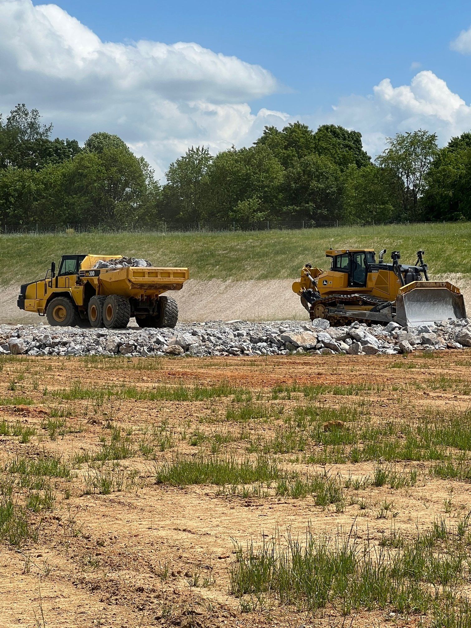 Dump truck and bulldozer scattering rocks throughout the site
