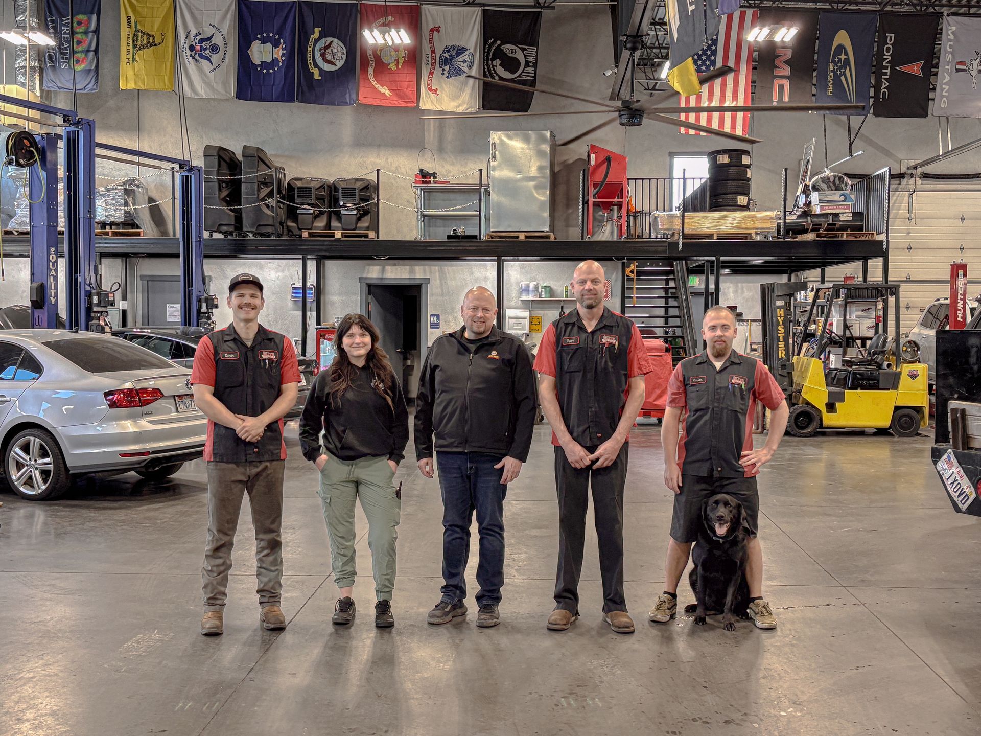 Group of auto shop employees posing for a photo; inside the shop with flags and a car lift.
