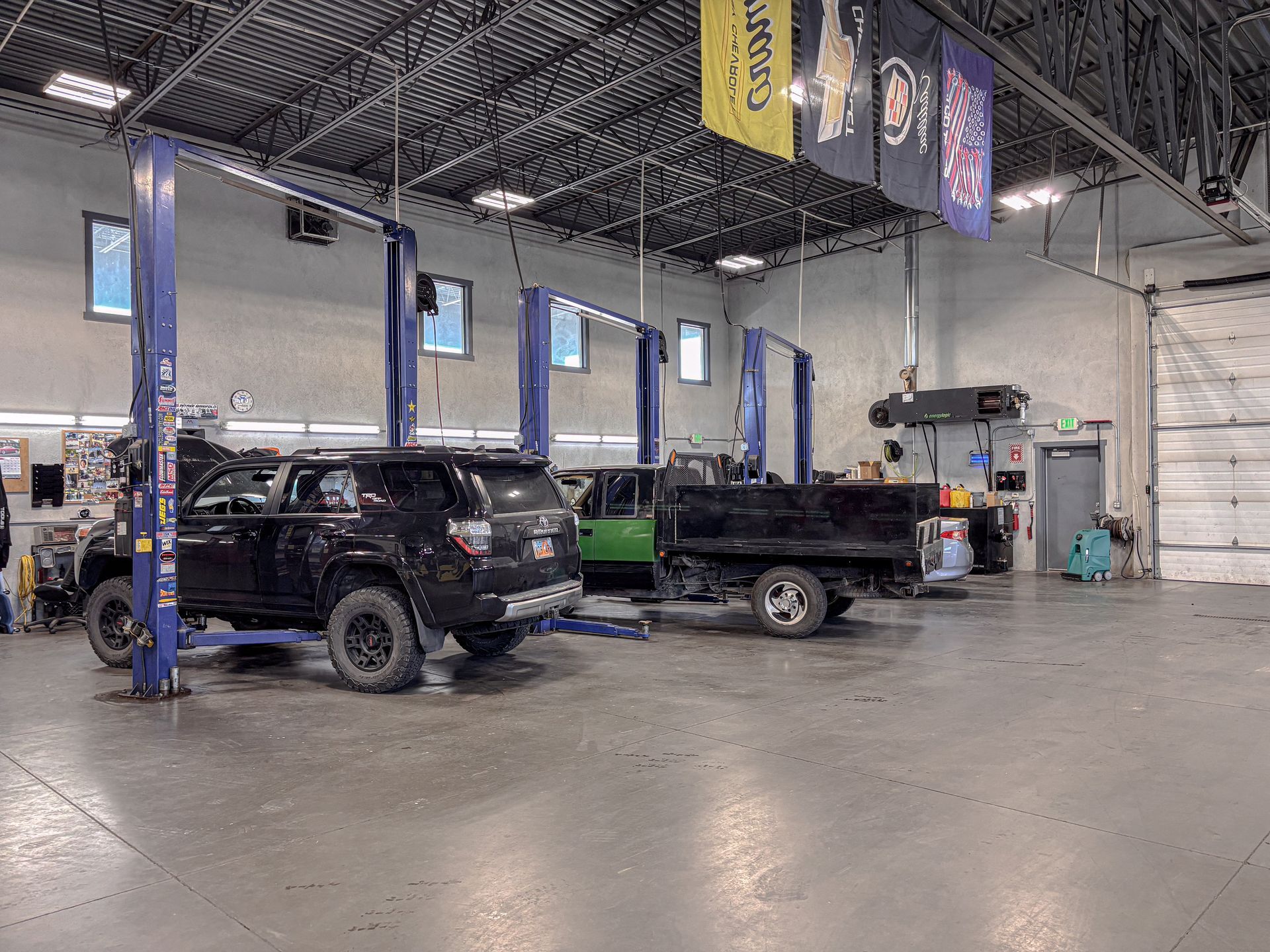 Garage interior with several vehicles on lifts, including a black SUV and a green truck.
