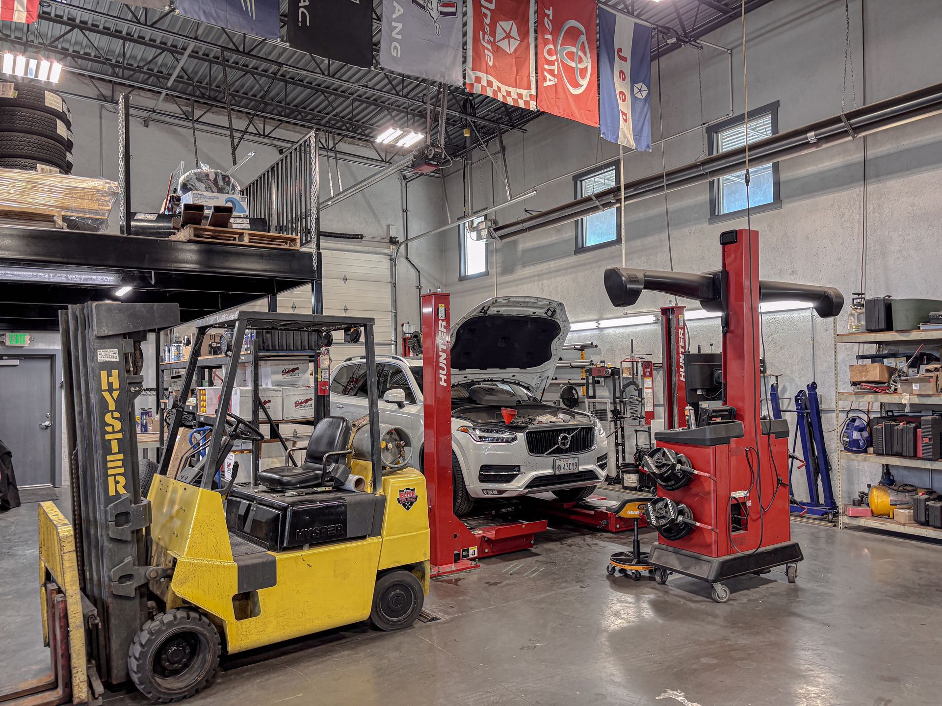 A yellow forklift and car on a lift in a car repair shop.