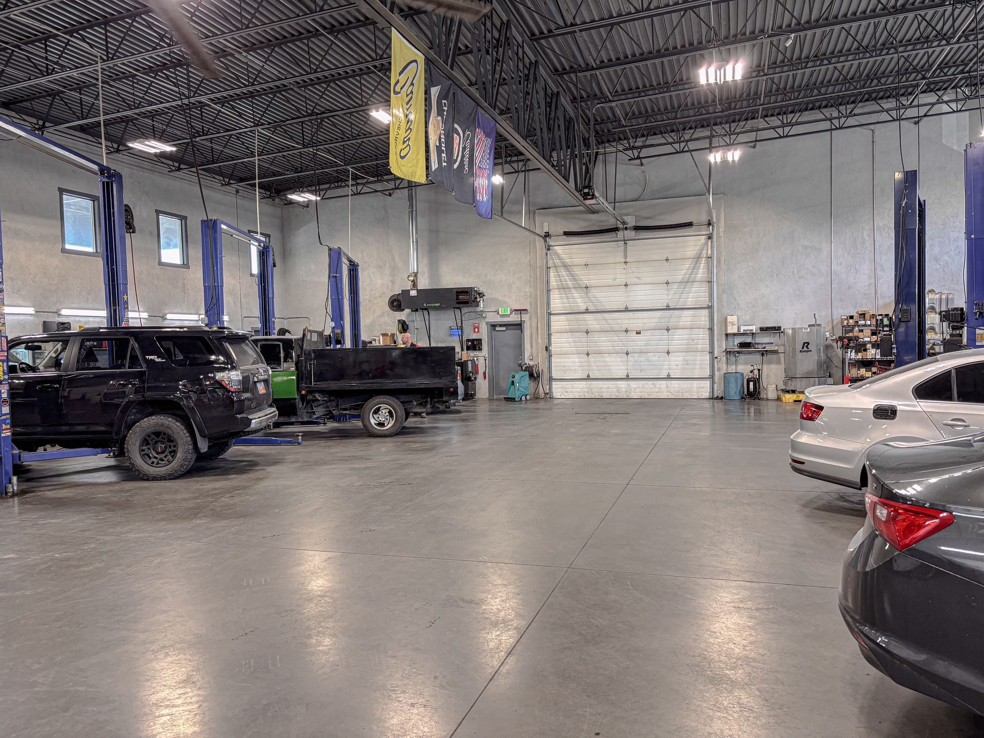 Interior of a car repair shop. Cars on lifts and parked on the floor, concrete floor, and open bay door.