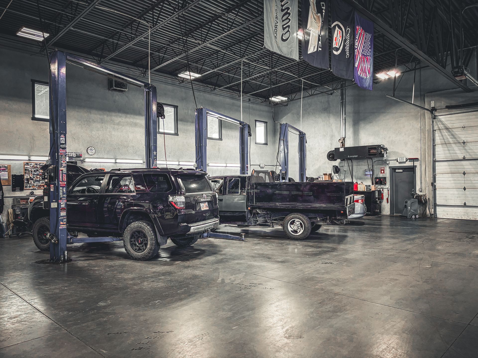 A workshop with vehicles on lifts: a black SUV, a pickup truck, and a utility truck.