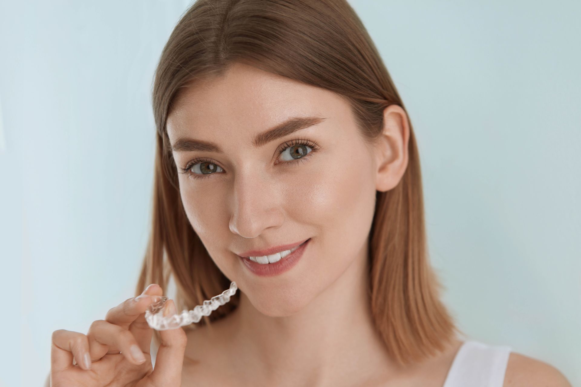 Woman smiling while holding a pearl necklace against a light background