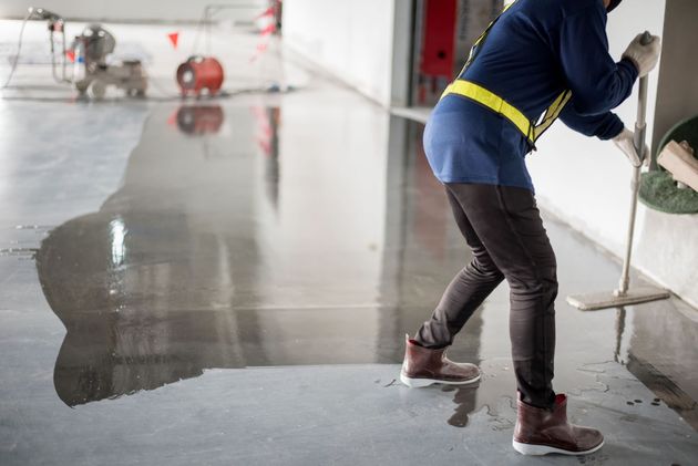 Worker spreading wet concrete on a floor with a squeegee in an indoor construction site.