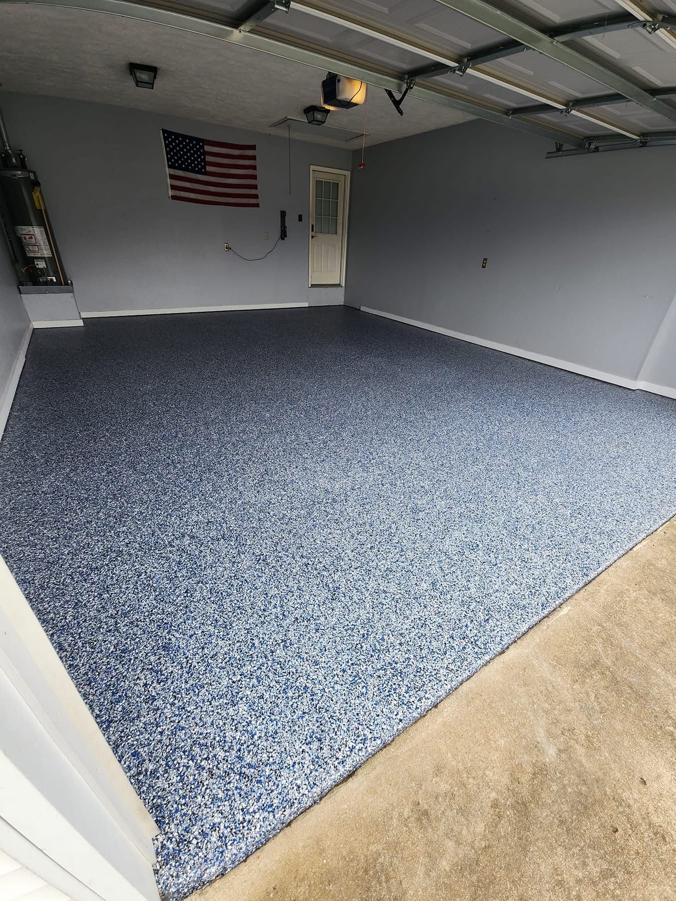 Empty garage with gray walls, blue carpet, and an American flag on the back wall.