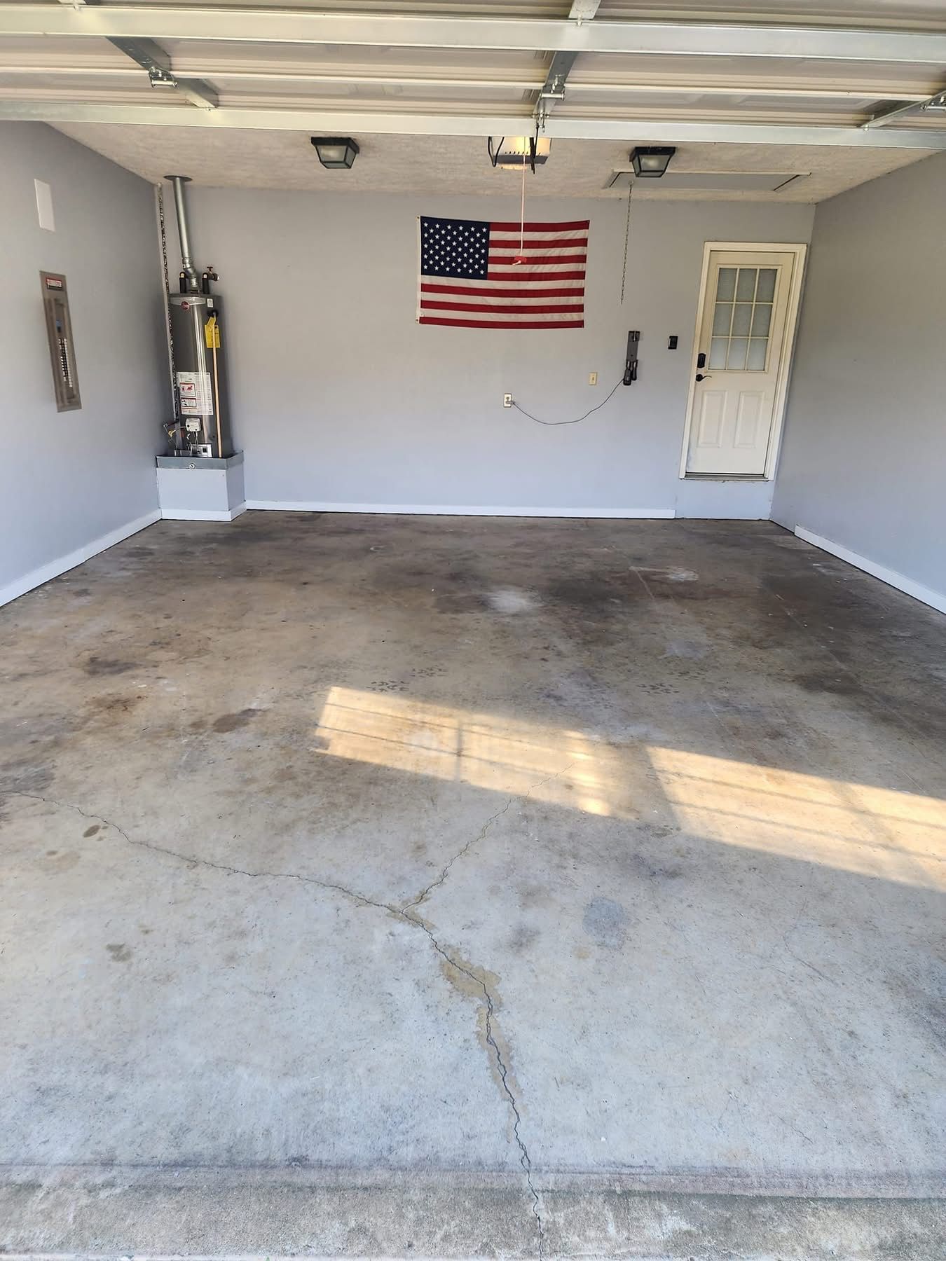 Empty garage with cracked concrete floor, American flag on back wall, and a white side door.