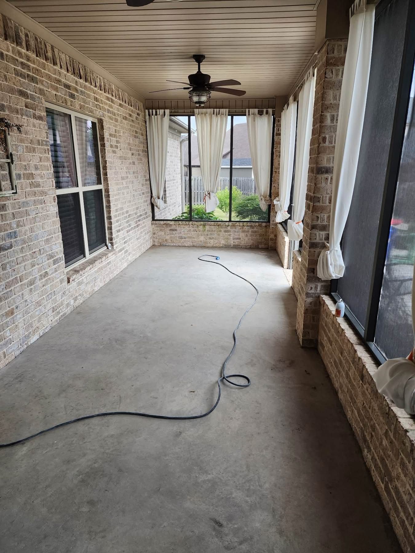 Covered porch with stone walls, concrete floor, ceiling fan, and a loose black cord running across it.