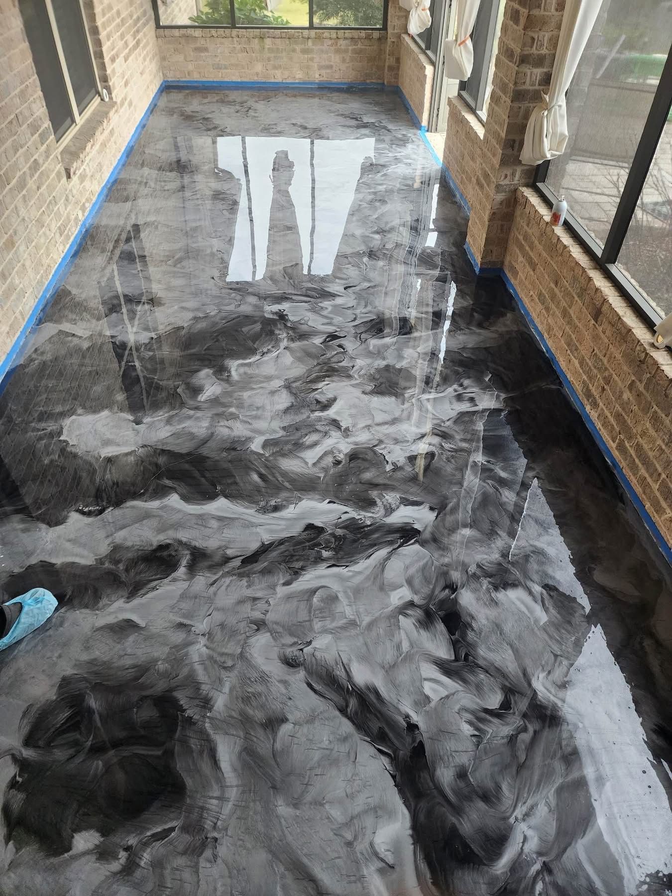 Covered porch floor with black-and-white marbled epoxy finish and blue painter’s tape along the edges.