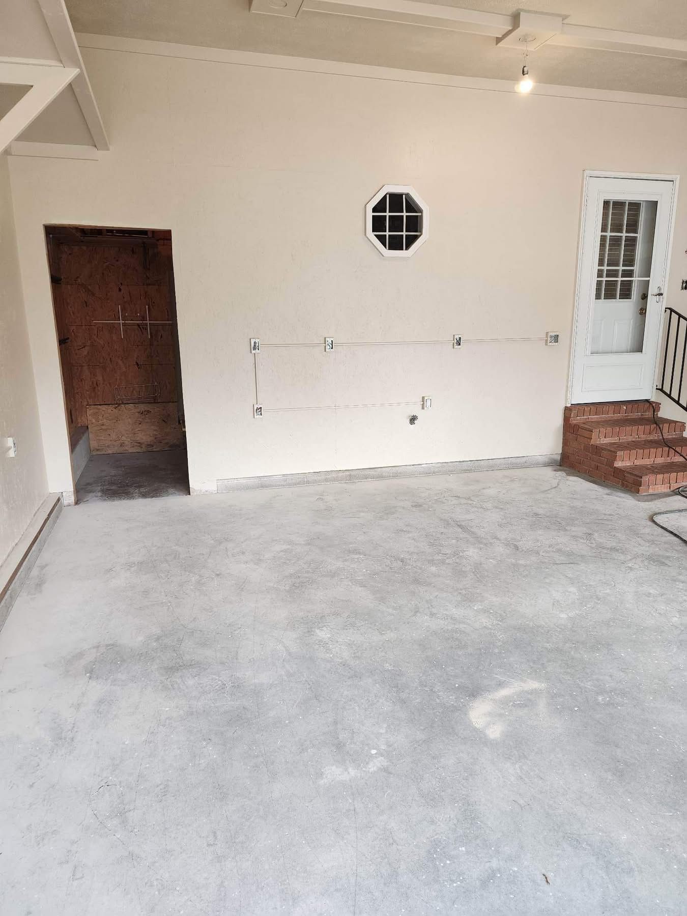 Empty garage interior with unfinished concrete floor, white walls, brown door, and small octagonal window.