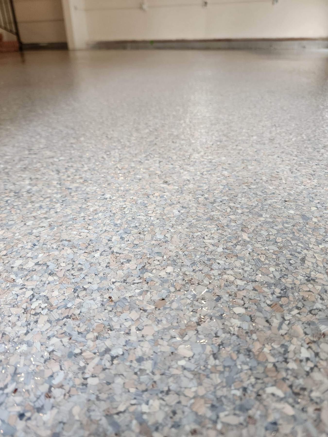 Close-up of a speckled terrazzo floor in a hallway with a blurred wall in the background