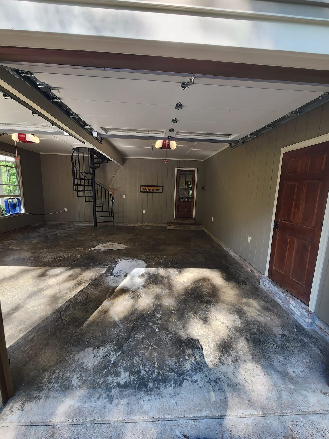 Empty garage interior with concrete floor, open door, and sunlight streaming in through the left side.