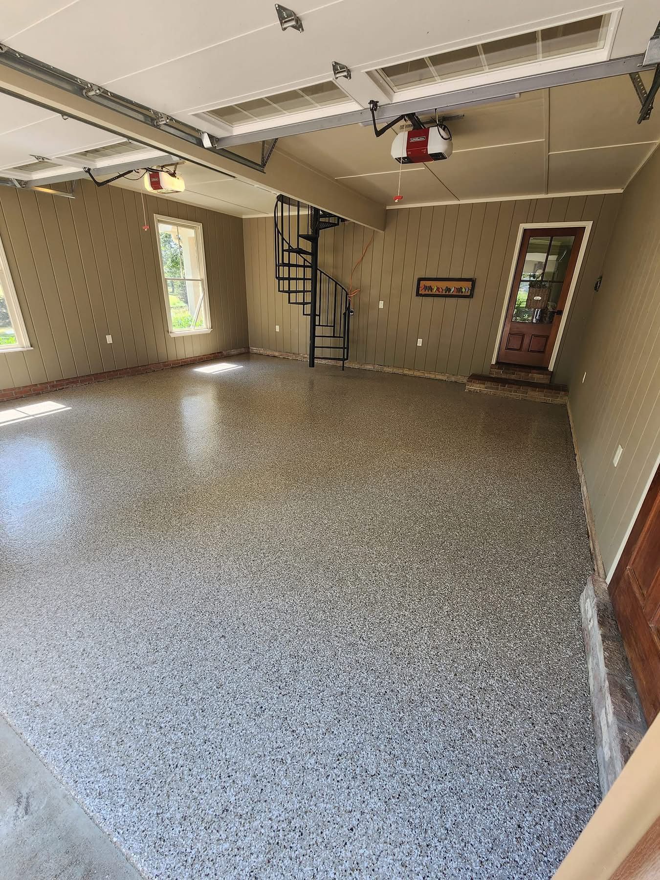 Empty garage interior with speckled floor, beige walls, overhead door opener, and side door.