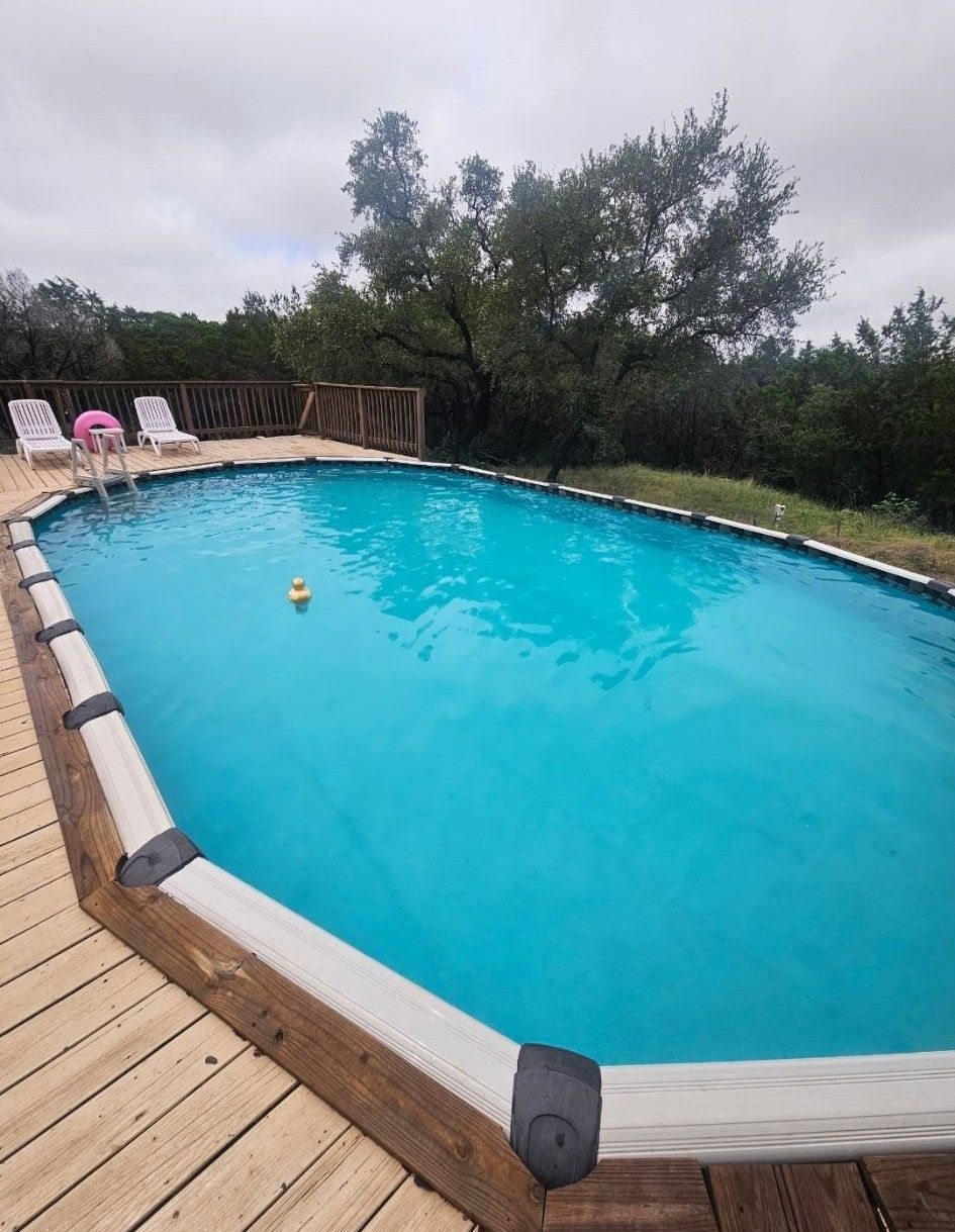 A large swimming pool surrounded by trees and a wooden deck.