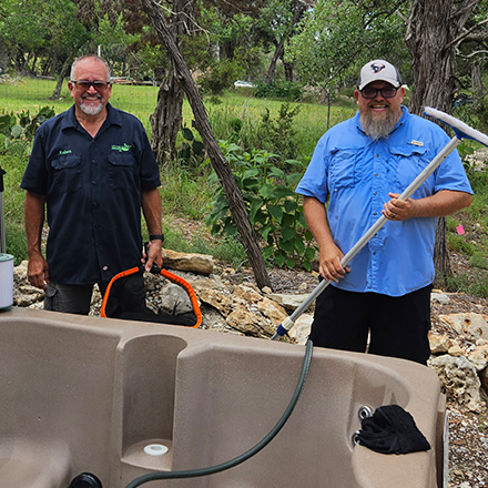 Two men are standing next to a hot tub with a hose attached to it.
