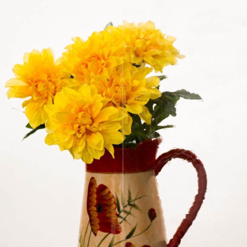 Yellow flowers in a red-and-cream ceramic pitcher with a floral design