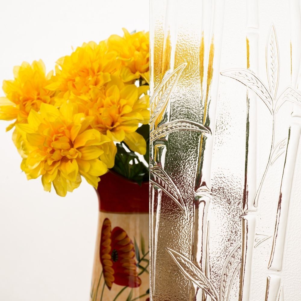 Yellow flowers in a vase beside frosted glass with a leaf pattern