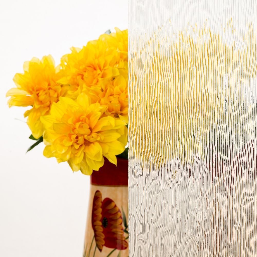 Bright yellow flowers in a vase beside frosted glass with vertical patterns