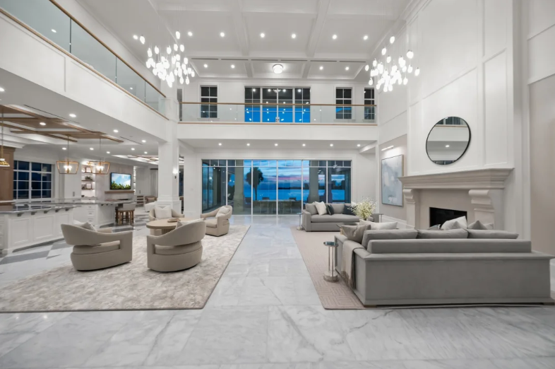 Spacious modern living room with white walls, gray sofas, chandelier, and large glass doors overlooking water.