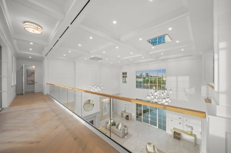 Bright white modern hallway with wood floors and glass railing overlooking a spacious interior below